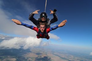 Un jeune homme fait un saut en parachute tandem et ouvre grand les bras pendant sa chute libre. 