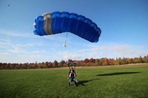 Un parachutiste freine un parachute bleu royal, alors que son passager tandem lève les jambes pour atterrir sur les fesses dans le gazon.