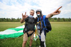 Un client tandem sourit fièrement en prenant une photo avec son instructeur de parachute qui le félicite après l'atterrissage.