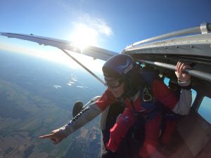 Une parachutiste novice accrochée à la barre de la porte de l'avion, à 13 500 pieds d'altitude, pointe l'école de parachutisme tout en bas, avant de sauter.