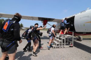 Un passager tandem souriant envoie la main à ses proches pendant que la file des parachutistes embarquent dans l'avion. 