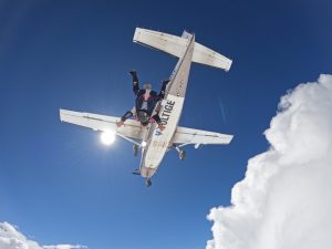 Le ventre d'un avion lettré Voltige survole de magnifiques nuages, alors qu'un instructeur de parachute tandem s'élance de la porte tête en bas.