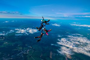Une équipe de vol relatif composée de 4 parachutistes sont en chute libre et tranchent sur un ciel de fin de journée bleu foncé.
