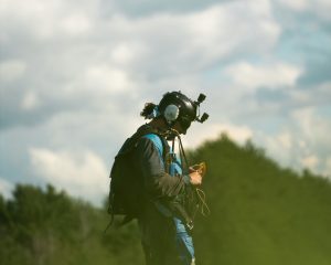 Un parachutiste caméraman debout dans un champ et portant encore ses caméras sur la tête range son équipement juste après son atterrissage.