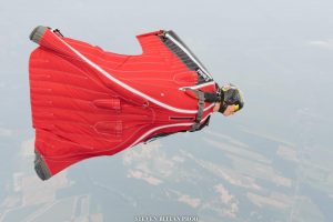 Une parachutiste vêtue d’une combinaison ailée rouge, performe un saut de wingsuit de compétition.
